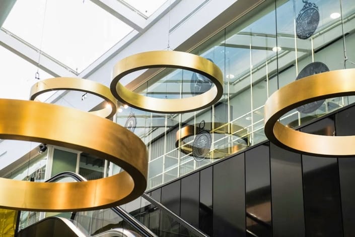 Luxurious gold circular light fixtures suspended from glass ceiling in London Stadium's premium hospitality area