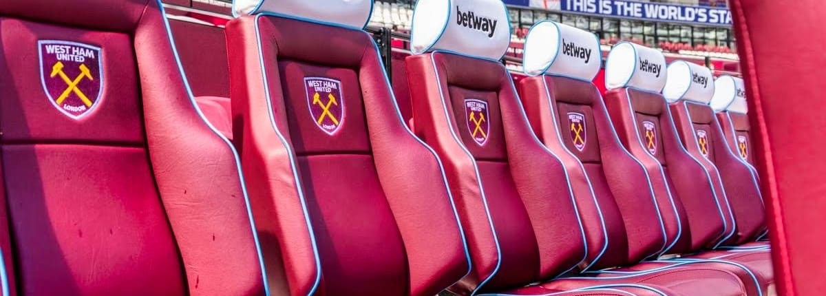 Premier League dugout with padded seats overlooking London Stadium pitch and home supporters section