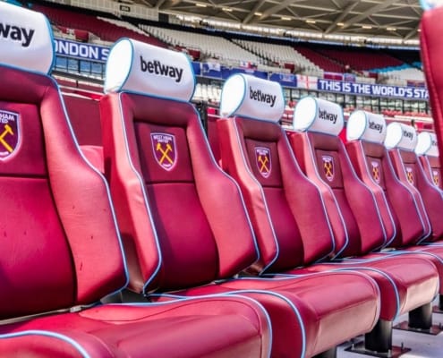 Premier League dugout with padded seats overlooking London Stadium pitch and home supporters section