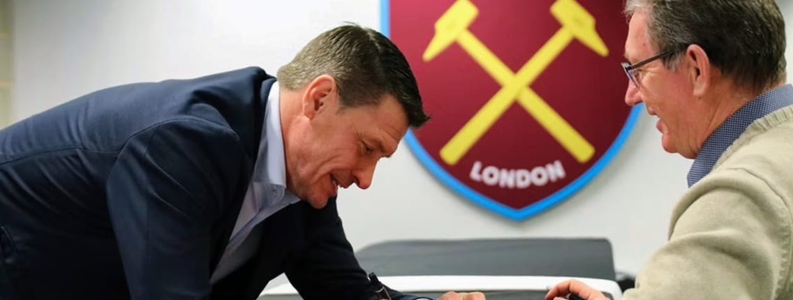 West Ham legend signing memorabilia with fan beneath club crest at London Stadium