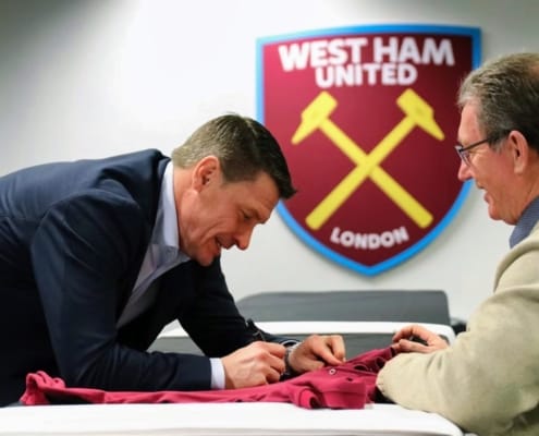 West Ham legend signing memorabilia with fan beneath club crest at London Stadium