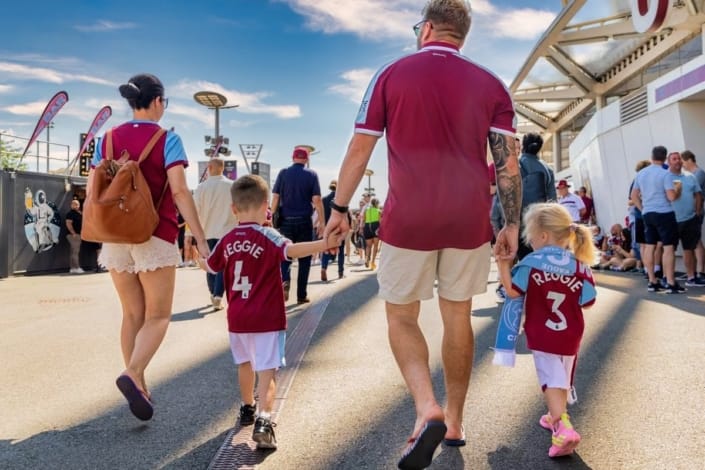 Family wearing West Ham United jerseys walking outside London Stadium with children in personalized shirts